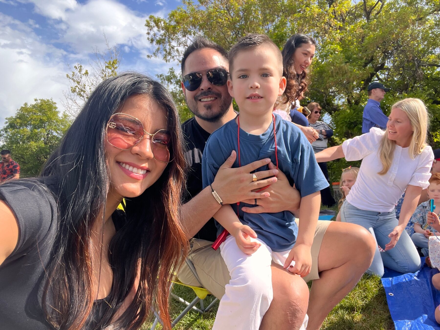 Oliver sitting with his parents at an outdoor gathering.